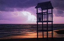 beach with rough sea and the wooden lookout tower at sunset.