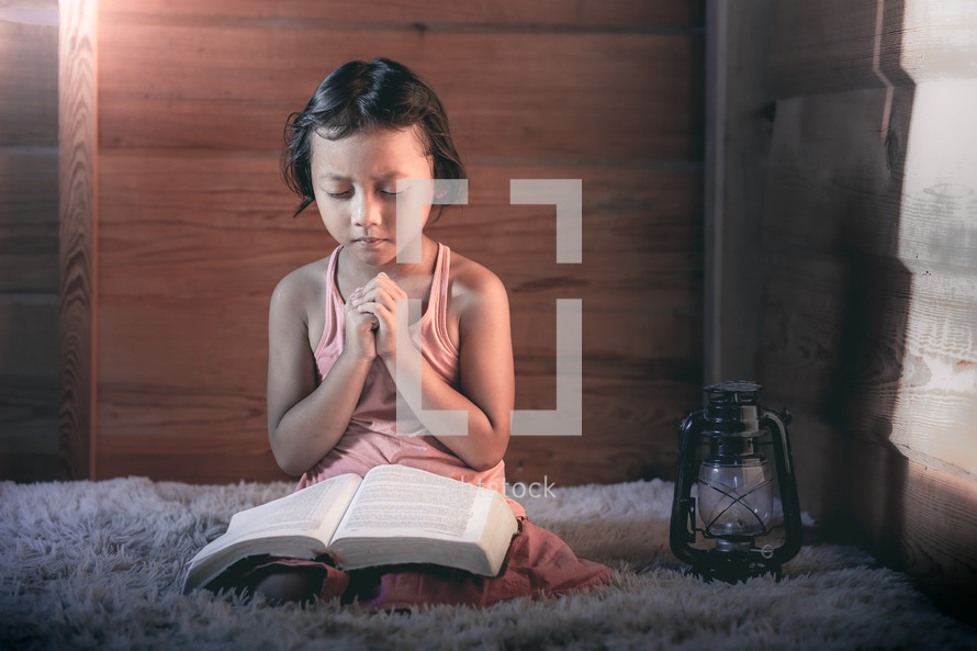 a little girl reading a Bible and praying 