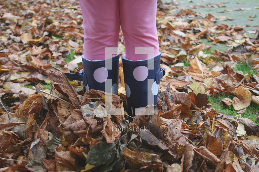 girl with rain boots in fall leaves 