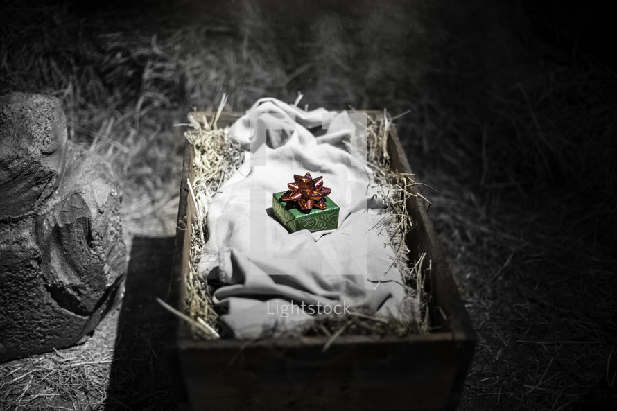 Green warpped box with red bow lying on linen cloth in hay-filled basket.
