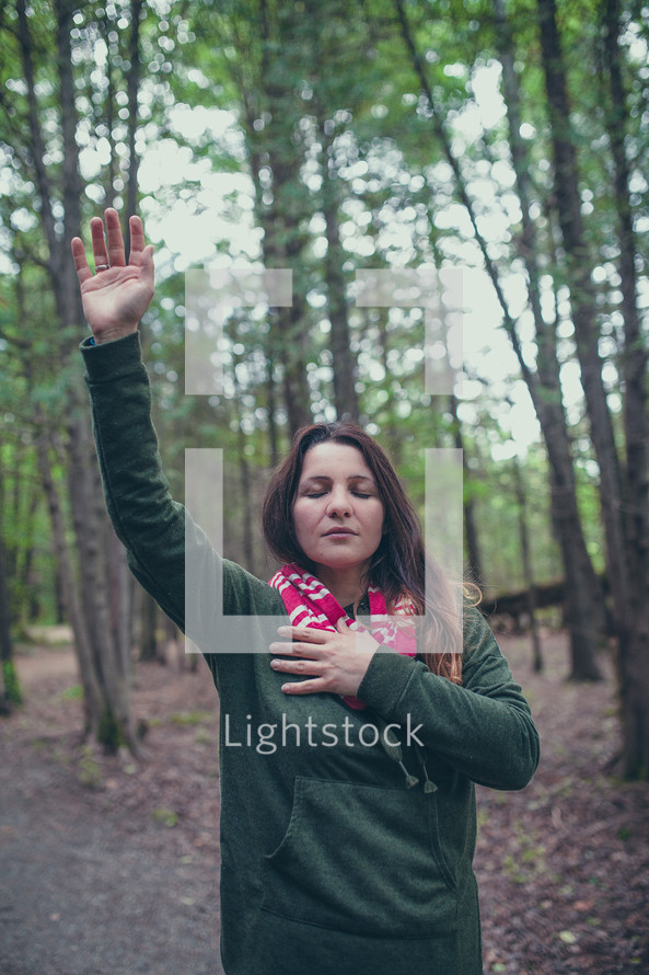 a woman with hand raised alone in a forest 
