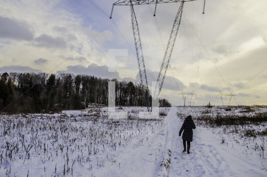 a person walking up a hill in snow under power lines 