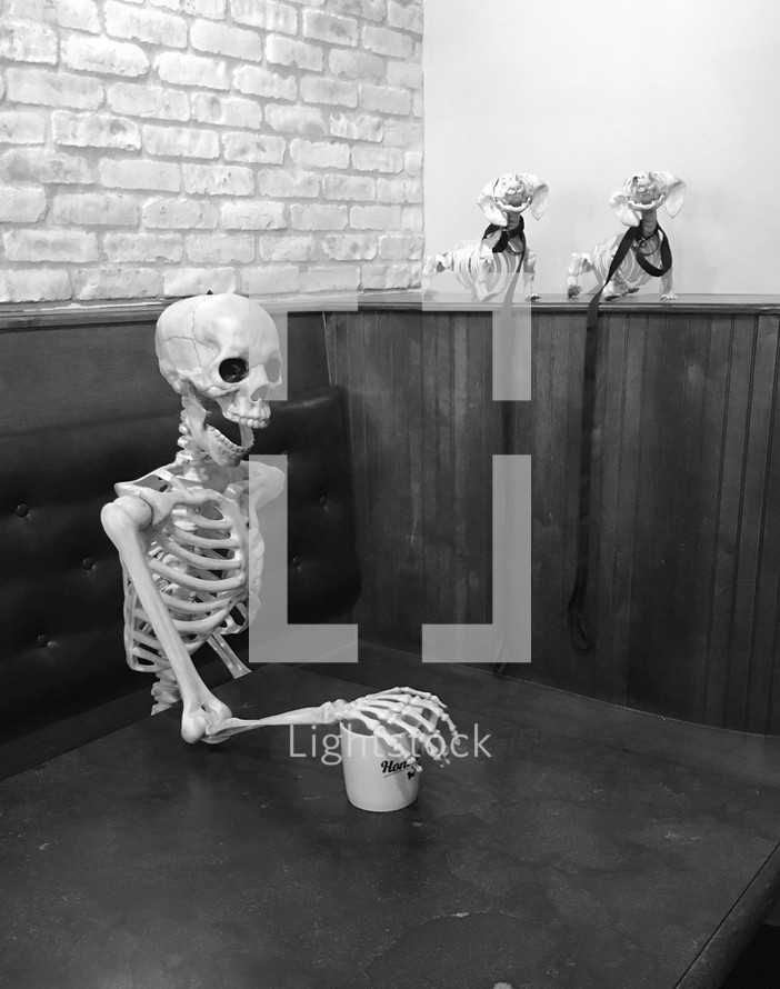 skeleton in a booth with arm on a mug 