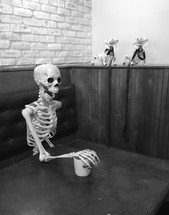skeleton in a booth with arm on a mug 