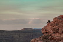 a couple sitting on a cliff at the edge of a canyon 