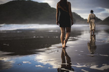 a woman following behind Jesus walking on a beach 