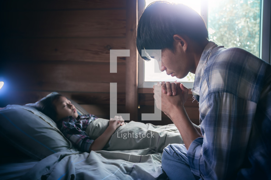 a sick boy lying in bed and praying father 