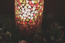 A colorful stain glass candle cover in a Christmas wreath