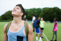 athletes standing on a sports field with backpack looking up to God