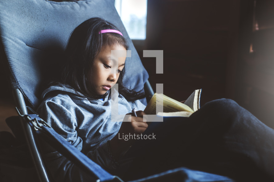 a girl reading a book sitting in a chair 