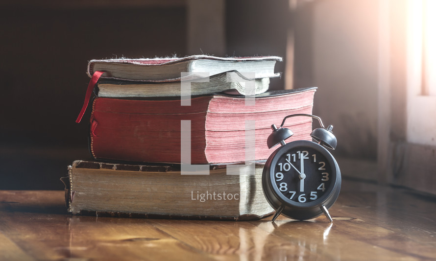 Clock and many Holy Bibles on wood table,