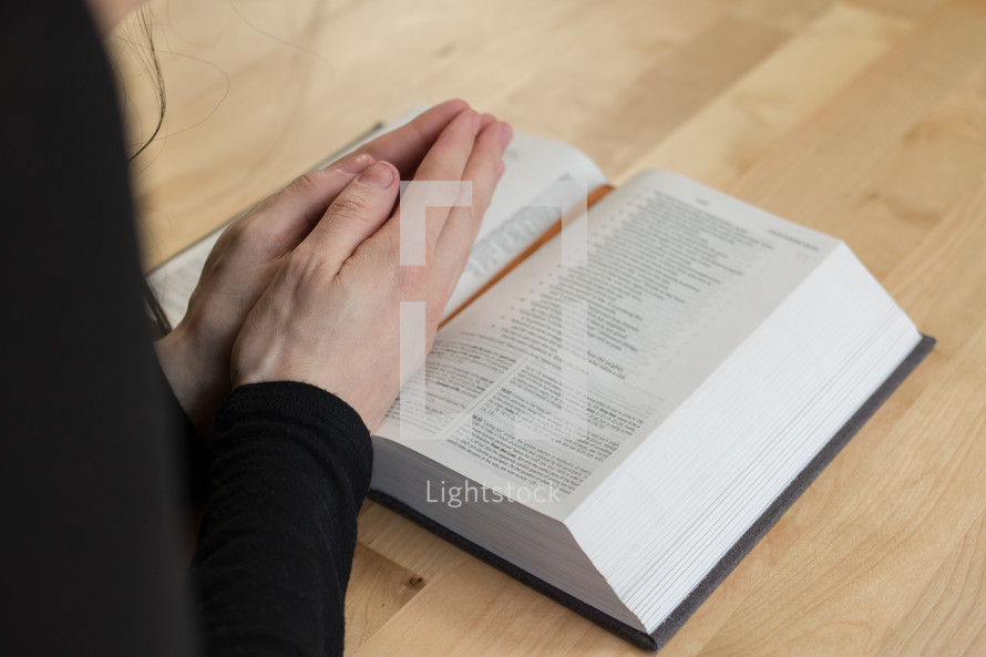 a woman with praying hands over the pages of a Bible 