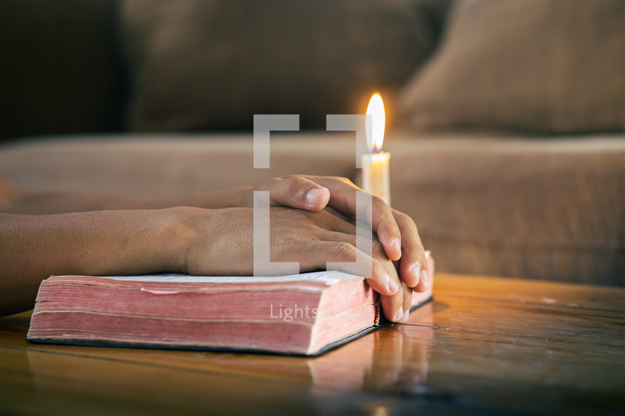 hands on a Bible with candlelight 