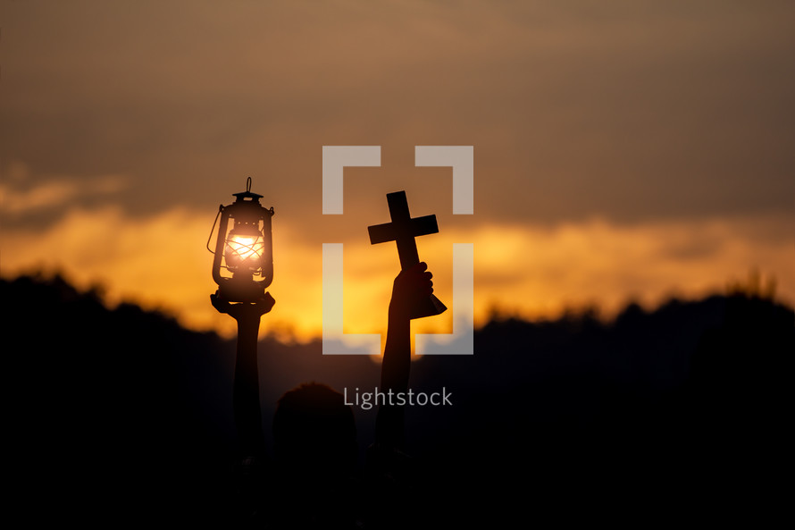 A boy praying to God with a cross and oil lamp at sunset 