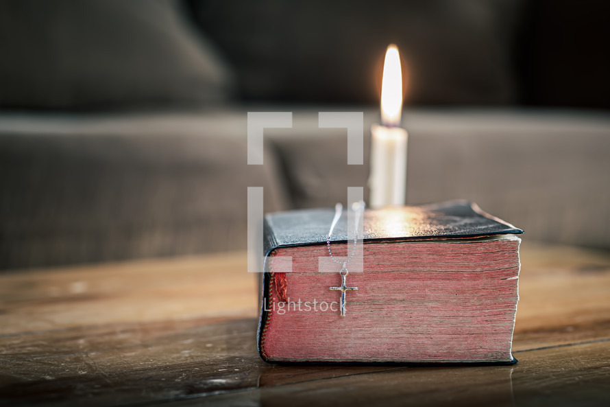 cross necklace on a Bible with candle 