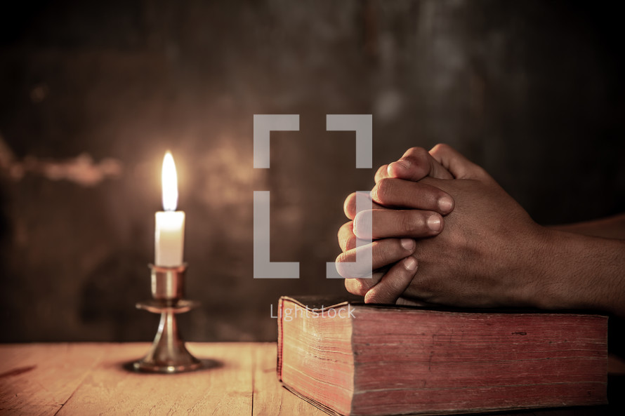 a man praying over a Bible in candlelight 