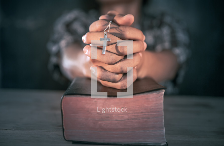 a cross necklace in praying hands over a Bible 