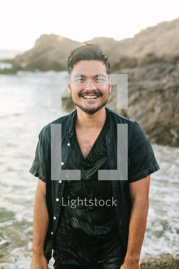 smiling man soaking wet standing on a shore 