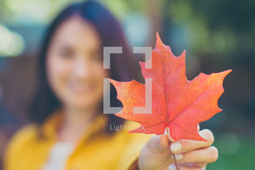 a woman holding a fall leaf