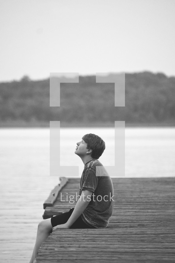 young man sitting on a dock looking up 