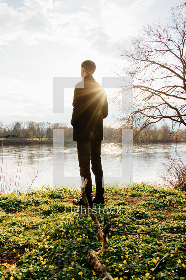 a man looking out at the water standing on a lake shore 