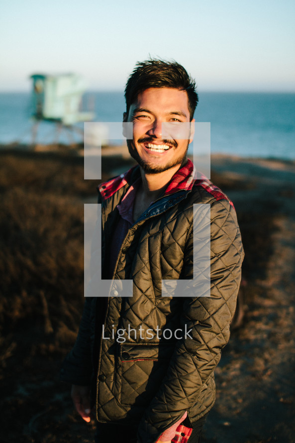 smiling man in a coat standing on a shore 