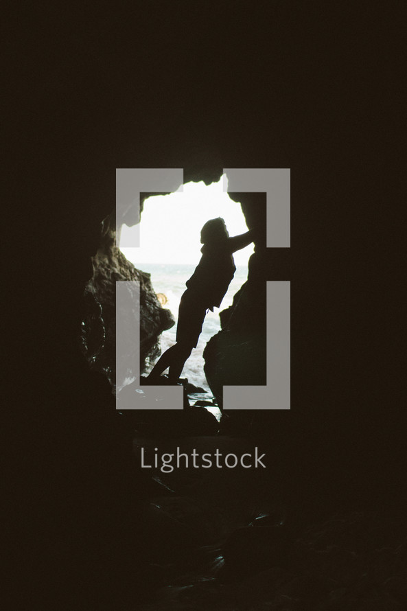 silhouette of a person at the mouth of a cave 