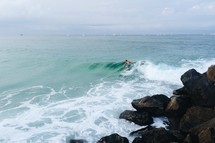 a man surfing near boulders in the ocean 