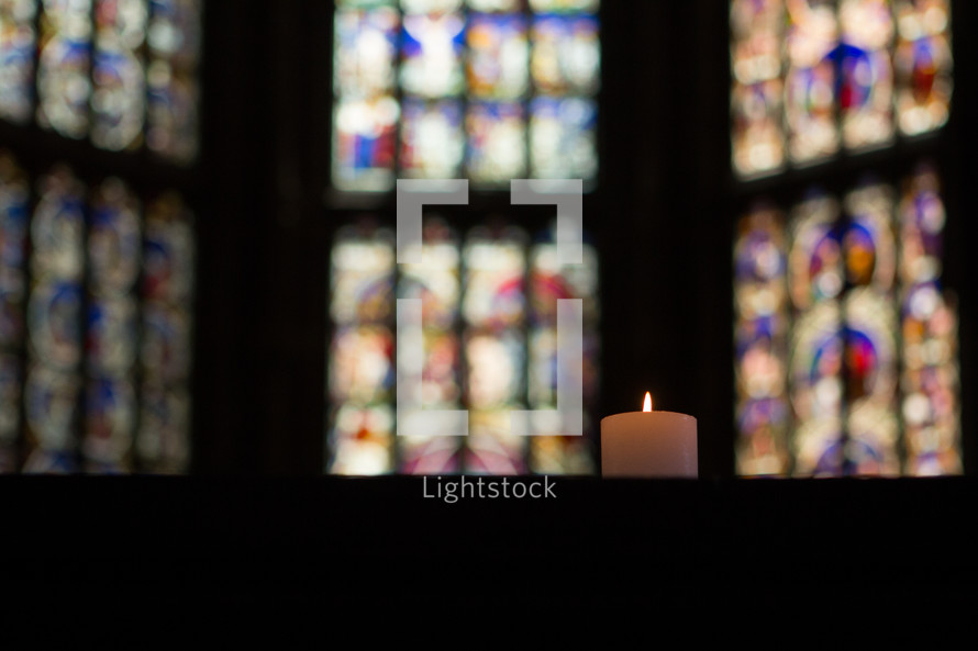 candle and a stained glass windows in a church 