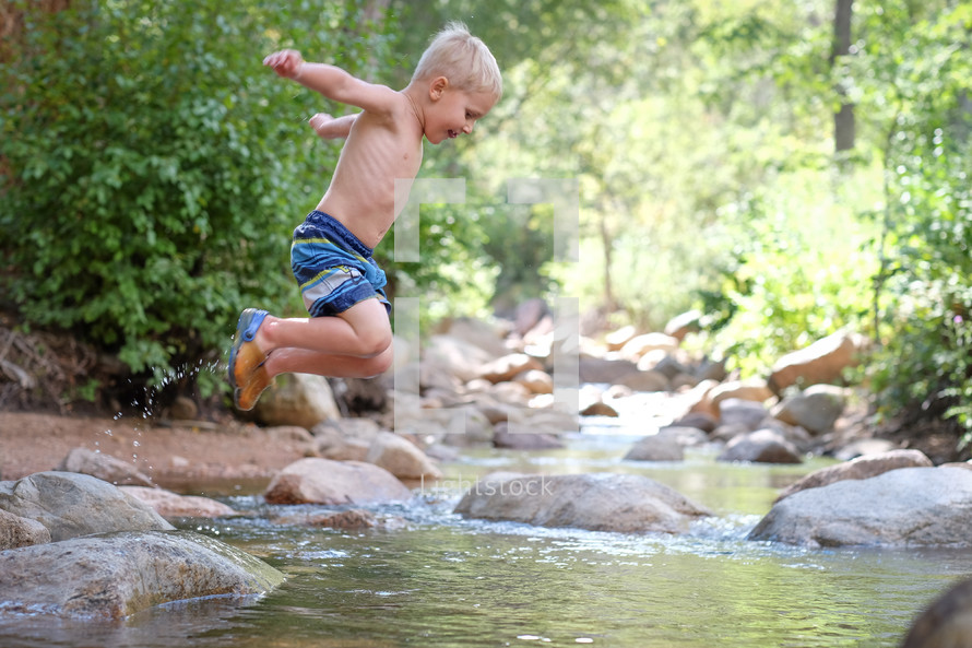 a boy child jumping into a stream in his swim suit 