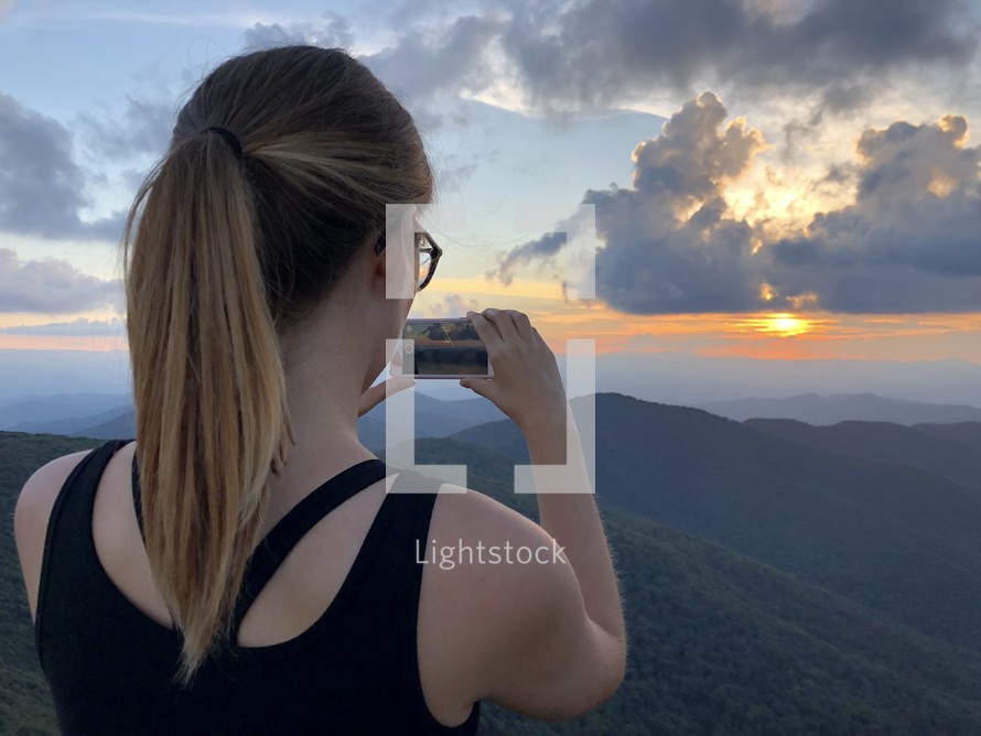 a woman taking a picture of the rising sun 