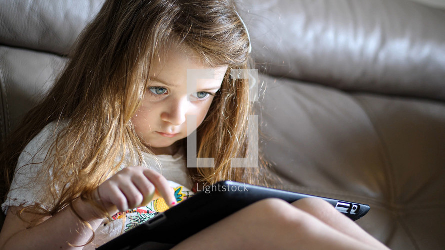 a little girl playing on a tablet 