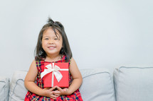 toddler girl in a Christmas dress holding a wrapped gift 