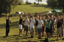 Teens standing outside at a camp with arms raised.