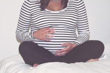 torso of a pregnant woman sitting holding her belly 