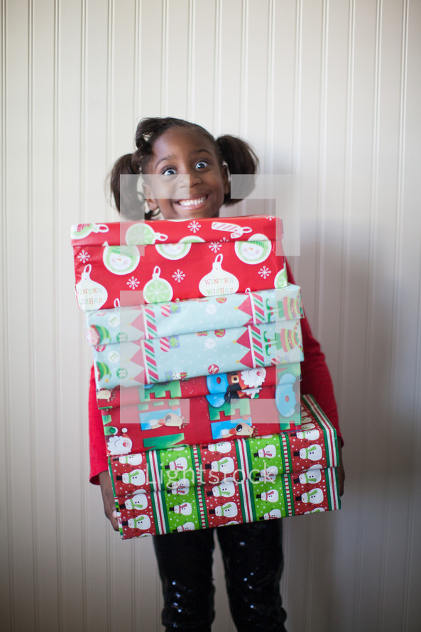 a girl child holding a stack of Christmas gifts 