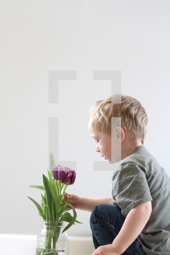 toddler boy touching flowers in a vase 