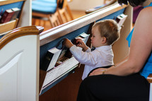 toddler boy playing with hymnals in the back of pews at church 