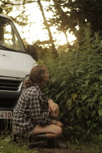woman kneeling in front of her truck looking at a plant 