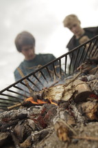 two young men cooking over a fire 