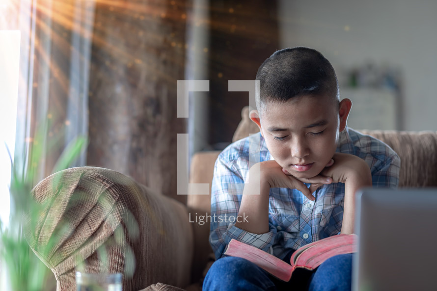 Young man sitting on a sofa and reading a bible at home