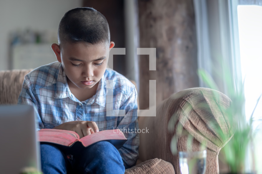 Young man sitting on a sofa and reading a bible at home