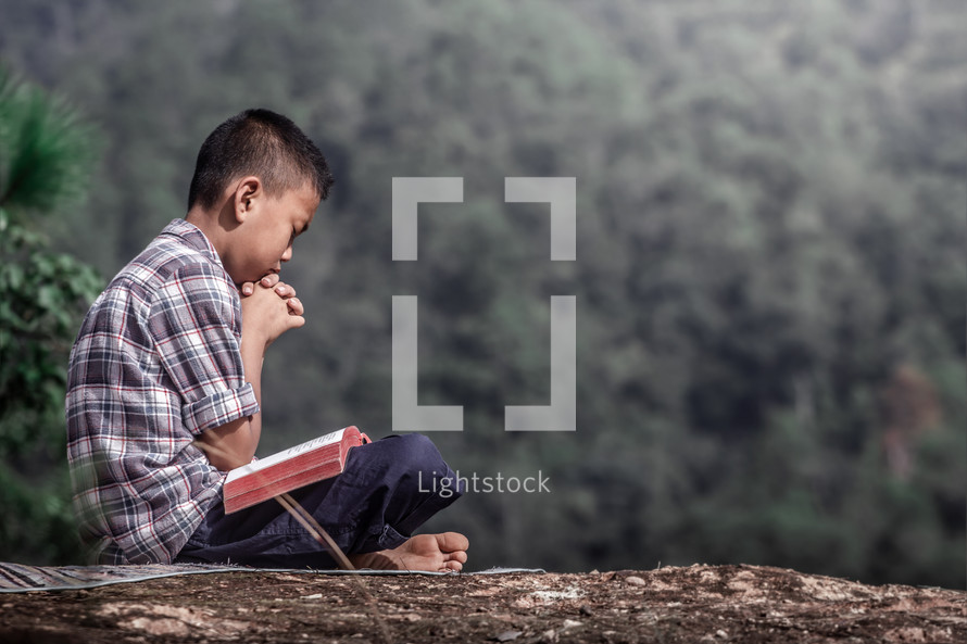 a boy sitting outdoors praying 