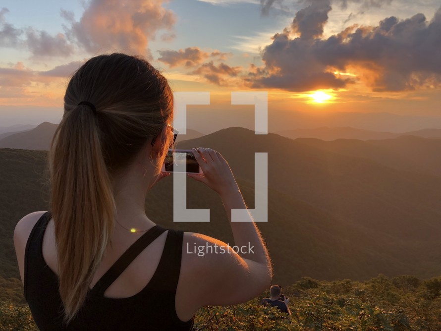 a woman taking a picture of the setting sun 
