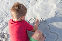 boy child drawing in the sand 