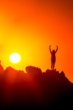 woman standing on a mountain at sunset with raised hands 