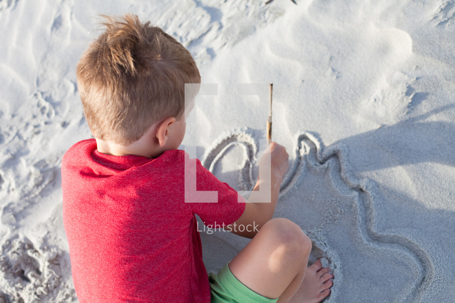 boy child drawing in the sand 