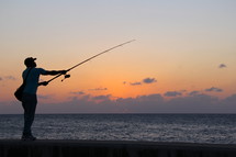 Man fishing on a beach at sunset 
