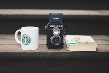 Starbucks mug, vintage camera, and book on a wood step 