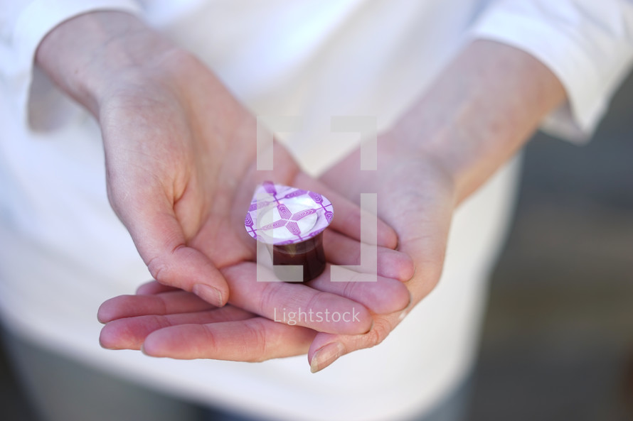 cupped hand holding a sealed communion wine cup